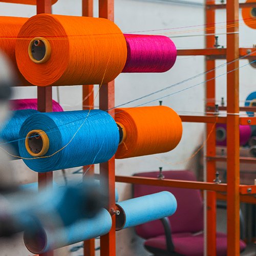 Gulungan benang PP (Polypropylene) Multifilament warna oranye muda, biru tomi, dan pink stabilo sebagai bahan baku produksi talikur
