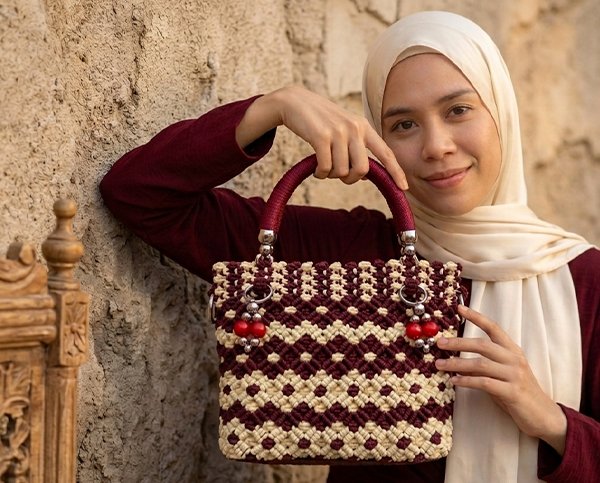 Tas kerajinan tangan dengan pegangan talikur berwarna marun dan anyaman bermotif krem serta merah marun.